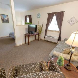 A cozy living room with a sofa, TV, and lamp, featuring brown curtains and a carpeted floor.