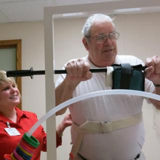 An elderly man participates in a physical therapy session with the assistance of a healthcare worker.
