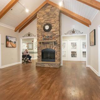 A spacious living room with a stone fireplace, vaulted ceiling with wooden beams, and hardwood flooring.