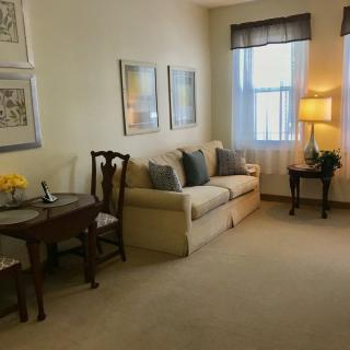 A cozy living room with a sofa, a small table with chairs, and a lamp by the window.
