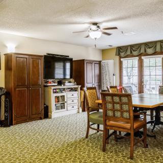 A cozy living and dining area with a carpeted floor, wooden furniture, and large windows.