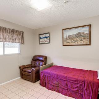 A cozy bedroom featuring a single bed with a maroon cover, a recliner chair, and framed artwork on the walls.