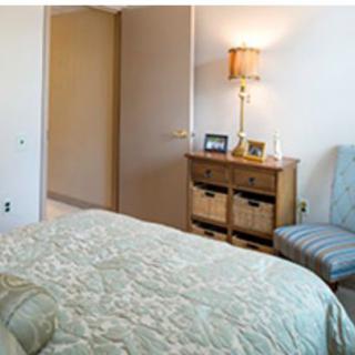 A cozy bedroom with a neatly made bed, a wooden chest of drawers, and a lamp providing warm lighting.