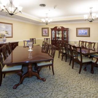 A traditional dining room with two long tables and matching chairs, featuring elegant chandeliers and a china cabinet.