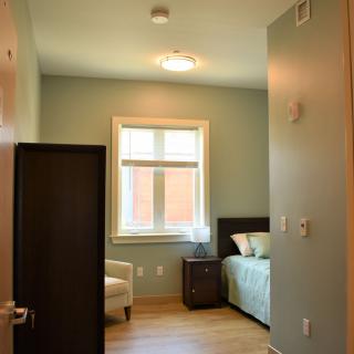 A cozy bedroom with a bed, nightstand, and armchair by the window.