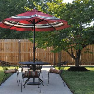 A cozy backyard patio set with an umbrella, table, and chairs under a tree.