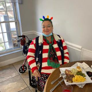 An elderly person enjoying a festive holiday meal, dressed in a colorful Christmas sweater and hat.