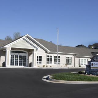 A suburban office building with a parking area in front, under a clear blue sky.