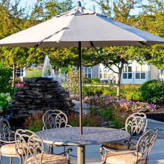 A sunny patio setting with a table, umbrella, and chairs surrounded by lush garden landscaping.
