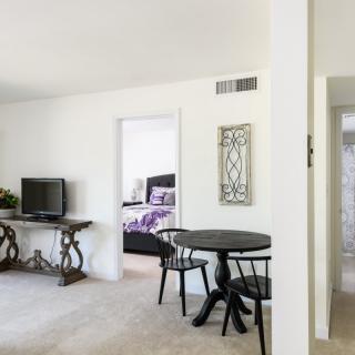 A cozy apartment interior featuring a living room with a TV, dining table with chairs, and a glimpse into the bedroom.