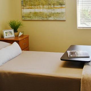 A minimalist bedroom setup with a neatly made bed, a side table with decor items, and a window letting in natural light.