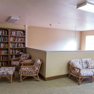 A cozy indoor reading area with bookshelves, cushioned wicker chairs, and a sofa.