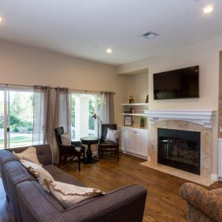 A cozy living room with a sofa and fireplace, featuring a wall-mounted television and large windows.