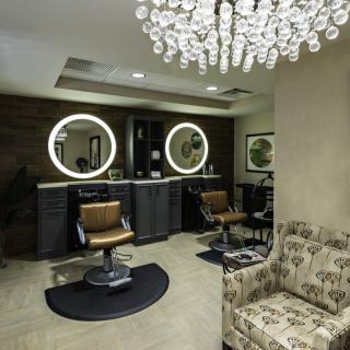 A luxurious salon interior featuring stylish chairs and illuminated mirrors.