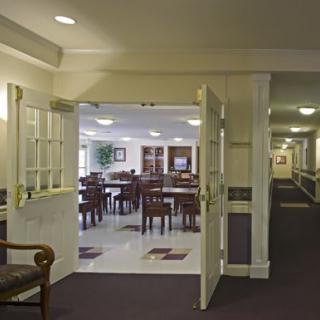 A view of a dining area from a hallway, featuring tables and chairs under ceiling lights.