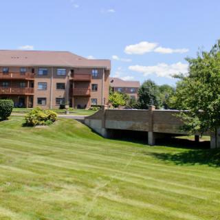 A scenic view of an apartment complex with a well-maintained lawn and surrounding trees under a clear blue sky.