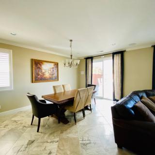 A modern dining room with a wooden table, chairs, and a chandelier, featuring a cozy seating area and artwork on the wall.