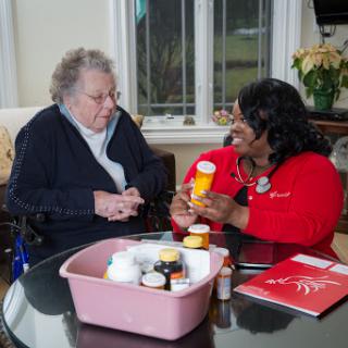 A caregiver discusses medication with an elderly woman, ensuring proper understanding and management of her health.