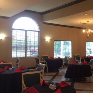 A well-lit restaurant dining area with neatly arranged tables, red napkins, and large windows.