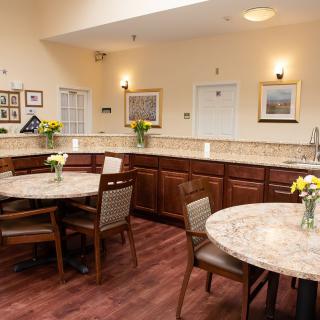 A cozy kitchen and dining area with round tables, chairs, and decorative flowers.
