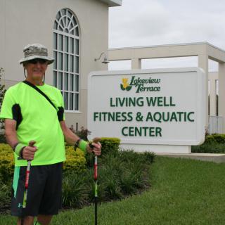 A person standing outside the Living Well Fitness & Aquatic Center holding walking poles.