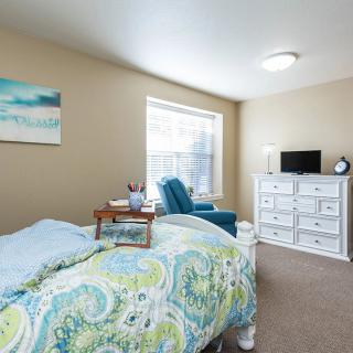 A cozy bedroom with a patterned comforter, armchair, dresser, and a small TV.