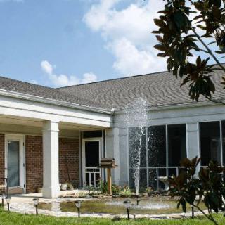A building with a small fountain in the garden under a clear sky.