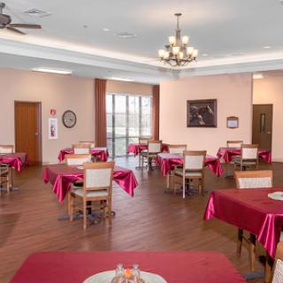 A spacious dining room featuring neatly arranged tables with red tablecloths, illuminated by a chandelier.