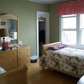 A cozy bedroom with a floral bedspread, wooden furniture, and a large window.