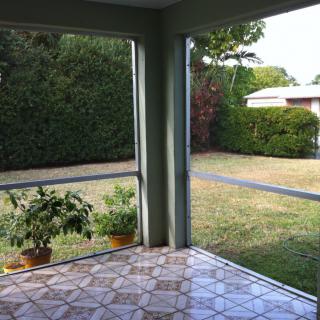 A screened porch overlooking a grassy backyard with potted plants.