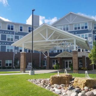 A large residential building with a covered entrance and landscaped front yard on a sunny day.