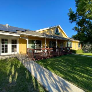 A sunny day view of a yellow house with solar panels and a patio.
