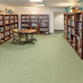 A quiet library room with shelves full of books and a table with chairs in the center.