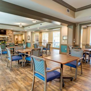 A spacious dining area with wooden floors, tables and chairs, well-lit by large windows.
