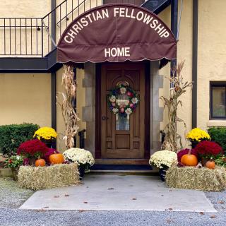 The entrance of a Christian fellowship home, adorned with autumn decorations including flowers, pumpkins, and hay bales.