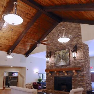 A cozy living room with a vaulted ceiling, featuring a brick fireplace and wooden beams, illuminated by chandelier lighting.