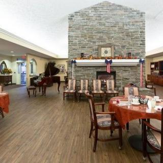 A cozy dining area with a stone fireplace, tables set for dining, and a piano in the corner.
