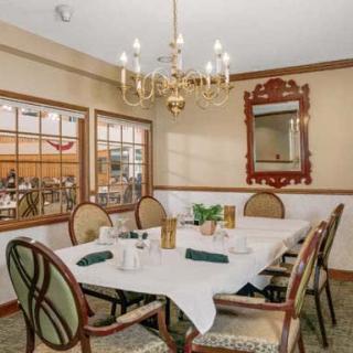 An elegant dining room with a set table, chandelier, and ornate mirror on the wall.