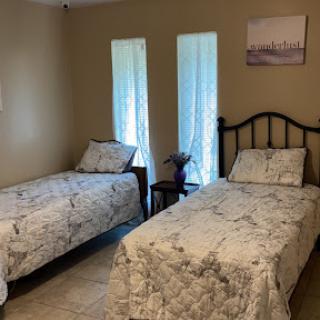 A cozy bedroom featuring two twin beds with decorative bedding and natural light coming through the windows.