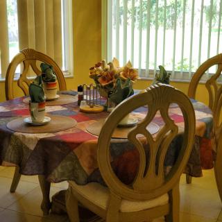 A cozy dining room with a colorful tablecloth and floral centerpiece, bathed in sunlight.