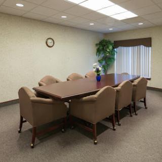 A spacious conference room featuring a large meeting table surrounded by comfortable brown chairs, complemented by a decorative plant and a wall clock.