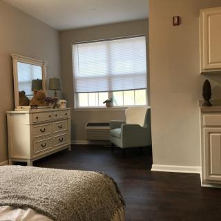 A cozy bedroom with a dresser, chair, and window.