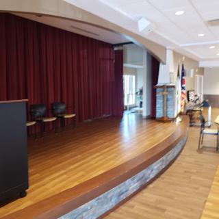 A view of a stage in an auditorium, featuring red curtains and a polished wooden floor.