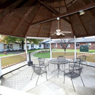 An outdoor gazebo with a table and chairs, surrounded by a garden area.