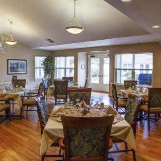 A well-lit dining area with neatly arranged tables and chairs, featuring elegant decor and hardwood flooring.
