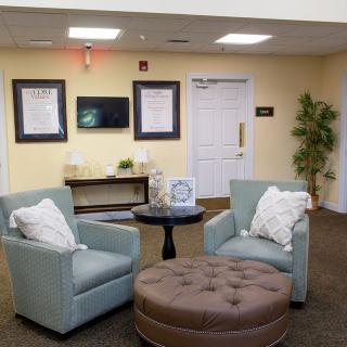 A cozy lobby area featuring two upholstered chairs, an ottoman, and a small table with decor.