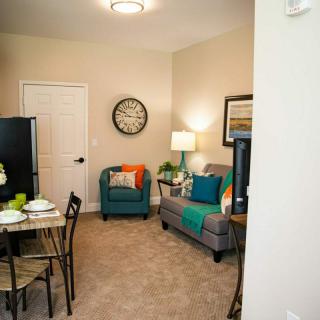 A cozy living room with a sofa, armchair, and dining table set against a neutral backdrop.