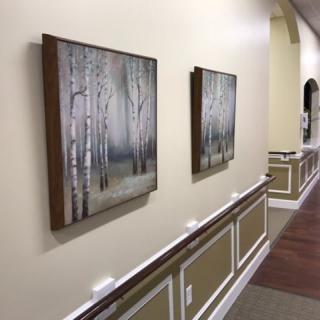 A hallway displaying two framed paintings of a woodland scene.