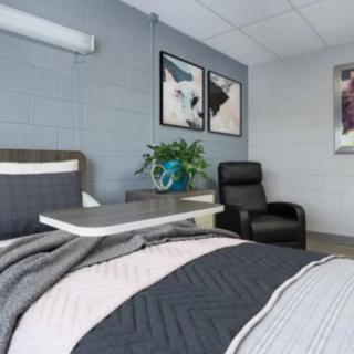 A modern bedroom featuring a neatly made bed, abstract artwork on the wall, a plant on the bedside table, and a comfortable chair.