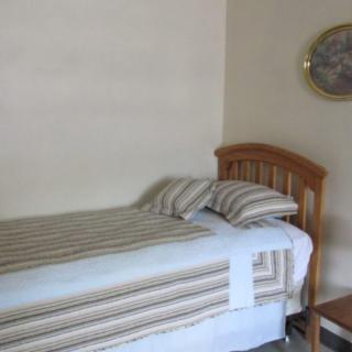 A simple bedroom setup with a single bed featuring striped bedding, a wooden headboard, and wall decor.